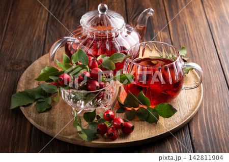 Rosehip tea in glass teapot and cup with fresh berries on wooden table background Rosehip tea in glass teapot and cup with fresh berries on wooden table background 142811904