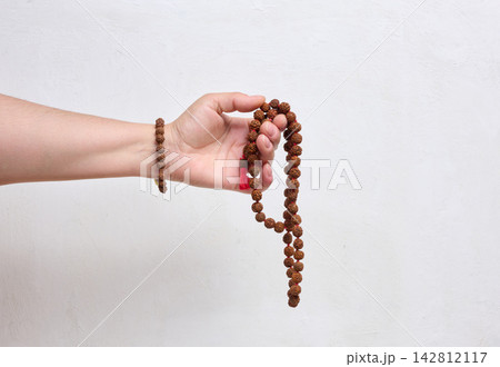 A person holding rudraksha prayer beads in their hand against a light background. A person holding rudraksha prayer beads in their hand against a light background. 142812117