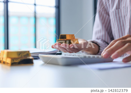 Investor hand using calculator for gold bar trading analysis. Concept for wealth management, asset protection, and financial planning. Investor hand using calculator for gold bar trading analysis. Concept for wealth management, asset protection, and financial planning. 142812379