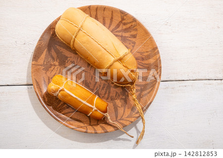 Provolone cheese, some smoked provolone cheeses made in Brazil placed on a ceramic plate, on rustic white wood, selective focus. 142812853