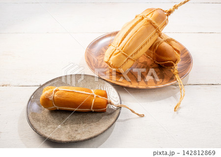 Provolone cheese, some smoked provolone cheeses made in Brazil placed on a ceramic plate, on rustic white wood, selective focus. 142812869