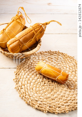 Provolone cheese, Some smoked provolone cheeses made in Brazil placed on straw utensils, on rustic white wood, selective focus. 142812874