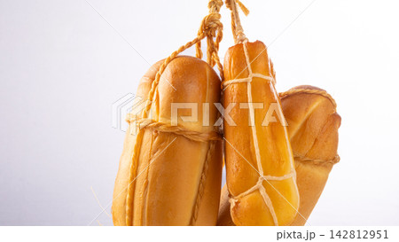 Provolone cheese, some smoked provolone cheeses made in Brazil hanging from ropes, white background, selective focus. Provolone cheese, some smoked provolone cheeses made in Brazil hanging from ropes, white background, selective focus. 142812951
