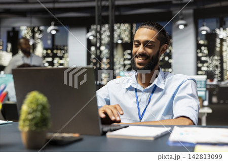 Smiling worker in office looking over paperwork on laptop, preparing quarterly revenue budget reports before deadline. Happy Arab man documenting company balance sheets and income statements Smiling worker in office looking over paperwork on laptop, preparing quarterly revenue budget reports before deadline. Happy Arab man documenting company balance sheets and income statements 142813099