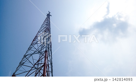 Towering telecommunication tower against a bright blue sky background, lattice steel structure design of transmitter antenna, cell site tower for mobile network signal and communication technology, pe Towering telecommunication tower against a bright blue sky background, lattice steel structure design of transmitter antenna, cell site tower for mobile network signal and communication technology, pe 142814093