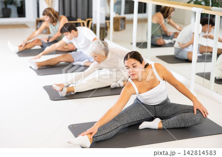 Positive young female performing set of exercises on a pilates mat during group class in fitness studio. 142814583