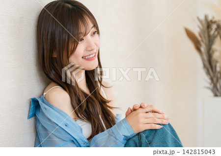 壁にもたれて笑顔を見せる女性。カジュアルファッションでくつろぐ明るいライフスタイル 142815043