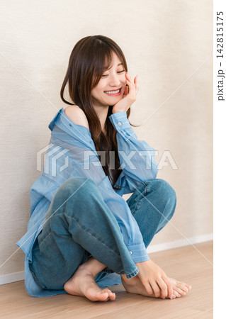 ブルーシャツとデニムを着こなし笑顔で座る女性。爽やかなカジュアルファッション 142815175