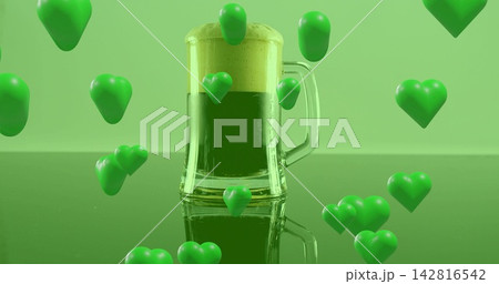 Displaying clear-glass mug holding green drink topped foam on studio table with floating hearts 142816542
