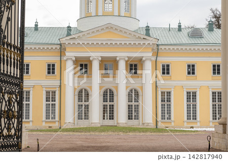 Historic yellow mansion features white columns and large windows, seen through ornate wrought iron gates in a landscaped garden area Historic yellow mansion features white columns and large windows, seen through ornate wrought iron gates in a landscaped garden area 142817940