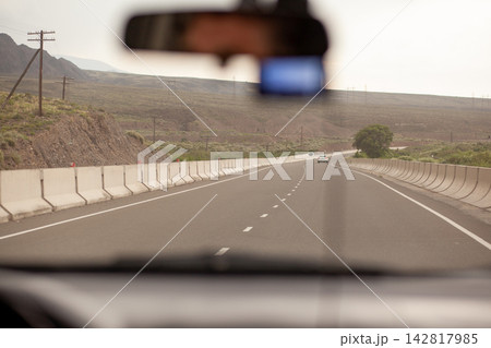 Perspective of a highway captured from inside a vehicle, showing a distant car and mountains along the roadside in a rural area 142817985