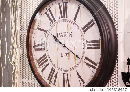 Vintage wall clock displays Roman numerals and the word Paris, set against a textured background with decorative elements enhancing its aesthetic 142818437