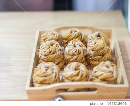 Handmade sweet pastries with intricate twisted designs are neatly arranged in a wooden tray, displaying a golden-brown color and appealing texture 142818608
