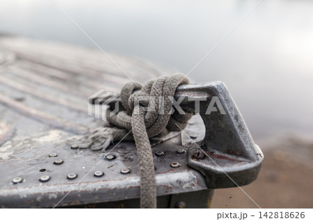 Close-up view of a weathered metal cleat with a rope knot secured tightly, situated on a boat dock with calm water in the background 142818626
