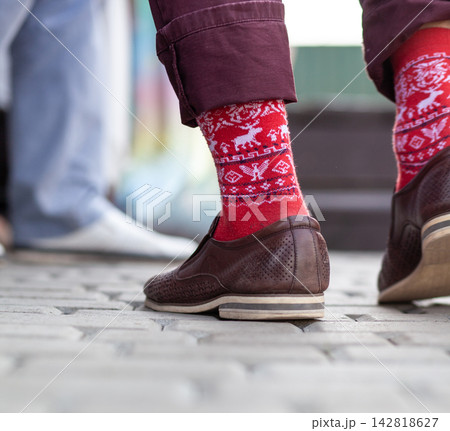 Close-up view of brown leather shoes paired with red socks displaying reindeer designs, with a vibrant urban backdrop visible in the scene 142818627