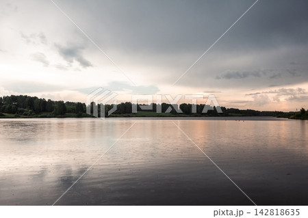 Tranquil view of a calm lake with reflections of cloudy skies and lush trees along the shoreline in a serene natural environment Tranquil view of a calm lake with reflections of cloudy skies and lush trees along the shoreline in a serene natural environment 142818635