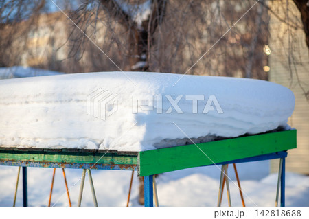 Flat surface covered with fresh snow on a colorful wooden structure, surrounded by trees and buildings in a winter outdoor environment 142818688