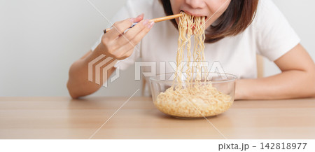 Happy young Asian woman enjoying a delicious bowl of hot instant noodles while relaxing at home, Cheerful female eating instant ramen with a smile at apartment. Simple lifestyle and quick meal concept Happy young Asian woman enjoying a delicious bowl of hot instant noodles while relaxing at home, Cheerful female eating instant ramen with a smile at apartment. Simple lifestyle and quick meal concept 142818977