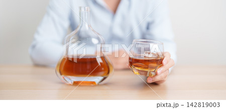 man with glass of cognac on table, suffering from alcohol addiction and alcoholism concept. depicting emotional distress, depression, substance abuse problem, unhealthy lifestyle and mental health 142819003