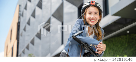 Morning outdoor motion An Asian businesswoman suited up and helmeted stands with her bicycle symbolizing the concept of a cheerful business commuter. Morning outdoor motion An Asian businesswoman suited up and helmeted stands with her bicycle symbolizing the concept of a cheerful business commuter. 142819146