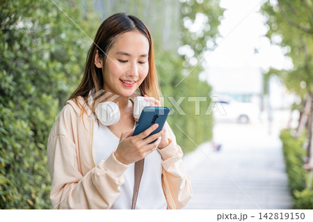 In an urban garden a happy young woman is seen dancing outdoors with wireless headphones fully engaged in selecting and enjoying her favorite energetic music. Her cheerful spirit is infectious. 142819150