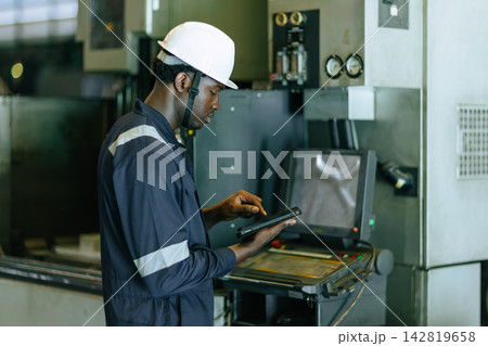 African Black Worker Engineer Monitors Machinery Operations in a Heavy industry Factory During Working Hours. African Black Worker Engineer Monitors Machinery Operations in a Heavy industry Factory During Working Hours. 142819658