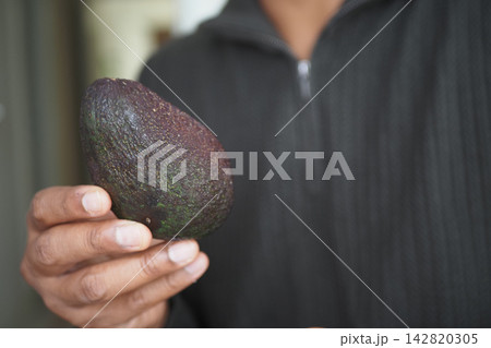 Man holding an avocado in a kitchen setting during the day 142820305