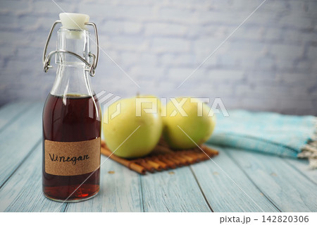 Glass bottle of vinegar with apples on wooden surface in kitchen Glass bottle of vinegar with apples on wooden surface in kitchen 142820306