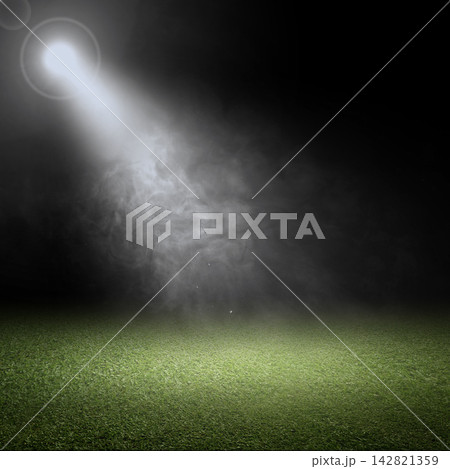 Bright spotlight shining down through smoke onto a green grass field at night. Smoke background 142821359