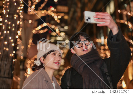 クリスマスのイルミネーションをスマートフォンで撮影する若いカップル クリスマスのイルミネーションをスマートフォンで撮影する若いカップル 142821704
