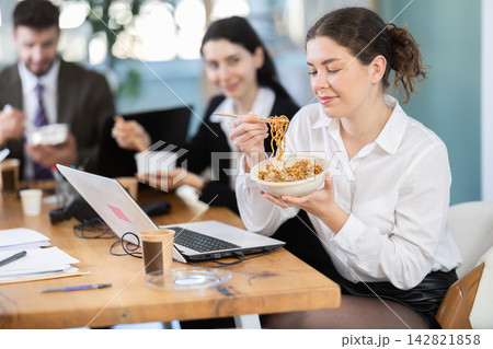 Lunch break - woman eating noodles with colleagues in modern office 142821858