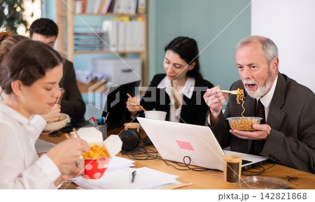 Group of colleagues, man and woman, are having lunch in office during their break, eating noodles Group of colleagues, man and woman, are having lunch in office during their break, eating noodles 142821868
