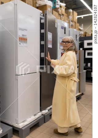 Senior woman considering refrigerators in a large retail appliance store Senior woman considering refrigerators in a large retail appliance store 142824107