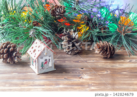 Small wooden toy house with a snowman design on a wooden table with pine branches and cones. Small wooden toy house with a snowman design on a wooden table with pine branches and cones. 142824679
