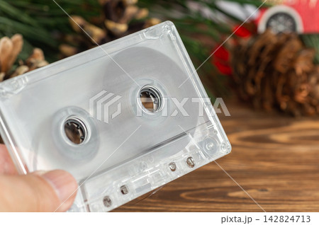 Hand holding a transparent cassette tape with a festive Christmas background of pine branches and cones Hand holding a transparent cassette tape with a festive Christmas background of pine branches and cones 142824713