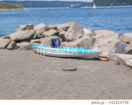 A blue recreational kayak with a life jacket parked on a rocky beach in Ruston, - June 13, 2026 Ruston WA, USA A blue recreational kayak with a life jacket parked on a rocky beach in Ruston, - June 13, 2026 Ruston WA, USA 142824756