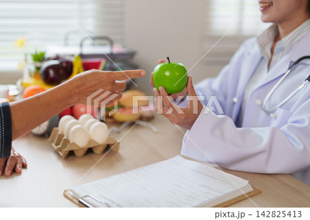 Doctor holding green apple during nutrition consultation with patient for healthy eating Doctor holding green apple during nutrition consultation with patient for healthy eating 142825413
