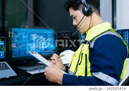 Asian engineer in a safety vest and headset analyzing clean energy HUDs and robotic automation interfaces in high tech industrial control room. Asian engineer in a safety vest and headset analyzing clean energy HUDs and robotic automation interfaces in high tech industrial control room. 142825414