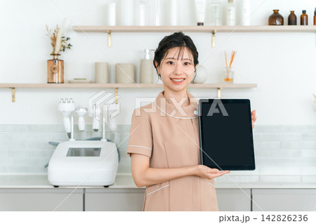 タブレット画面を見せる笑顔のエステティシャン。美容サロンのカウンセリングイメージ タブレット画面を見せる笑顔のエステティシャン。美容サロンのカウンセリングイメージ 142826236