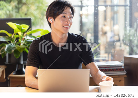 シェアオフィスでイヤホンを装着しオンライン会議に参加する若い男性 142826673