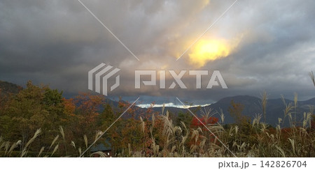 ススキと紅葉、雲の間から秋の山に沈む夕日 142826704