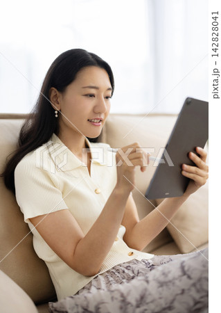 ソファに座りながらペンを使ってタブレットを操作する若い笑顔の日本人女性 ソファに座りながらペンを使ってタブレットを操作する若い笑顔の日本人女性 142828041