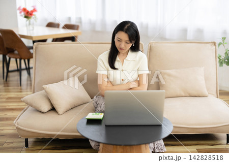 窓辺のソファでノートパソコンを見ながら腕組みをして首を傾げる若い日本人女性 窓辺のソファでノートパソコンを見ながら腕組みをして首を傾げる若い日本人女性 142828518