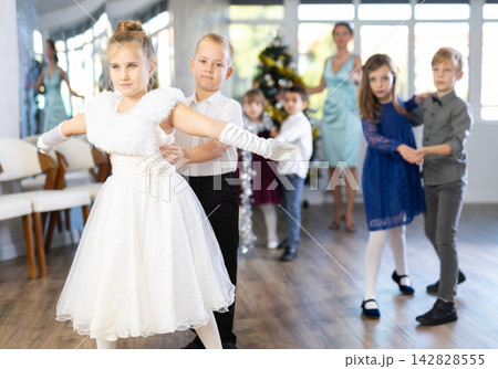 Preteen children in elegant outfits practicing partner dance in Christmas studio 142828555