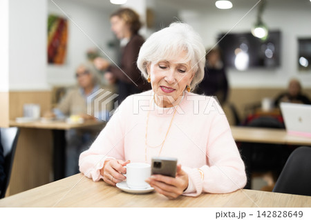 Woman sits at table in cafe and writes a message on her smartphone screen Woman sits at table in cafe and writes a message on her smartphone screen 142828649