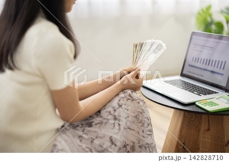 ノートパソコンを見ながら日本円の札束を数える女性の後姿 142828710