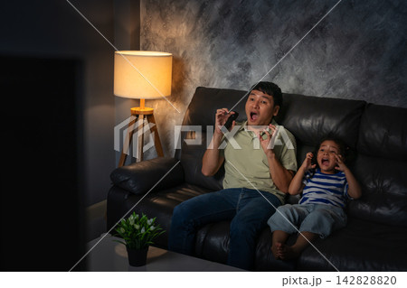 shocked and scared father and daughter watching horror movie tv in the living room at night shocked and scared father and daughter watching horror movie tv in the living room at night 142828820