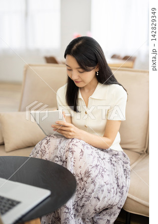 窓辺のソファでノートパソコンを見ながらノートにメモをする若い日本人女性 窓辺のソファでノートパソコンを見ながらノートにメモをする若い日本人女性 142829349
