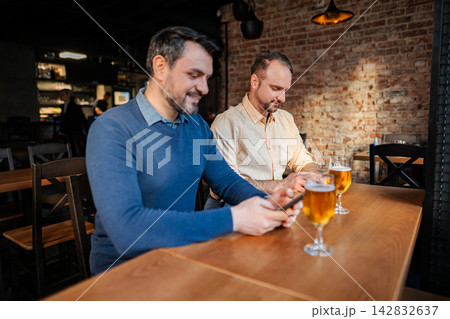 Two men focusing on smartphones while drinking beer at bar 142832637