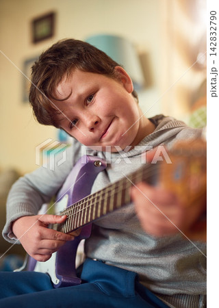 Boy, electric guitar and portrait in home for music or performance, learning or development with creativity. Male child, instrument and bedroom for education in house, hopeful musician with smile Boy, electric guitar and portrait in home for music or performance, learning or development with creativity. Male child, instrument and bedroom for education in house, hopeful musician with smile 142832790